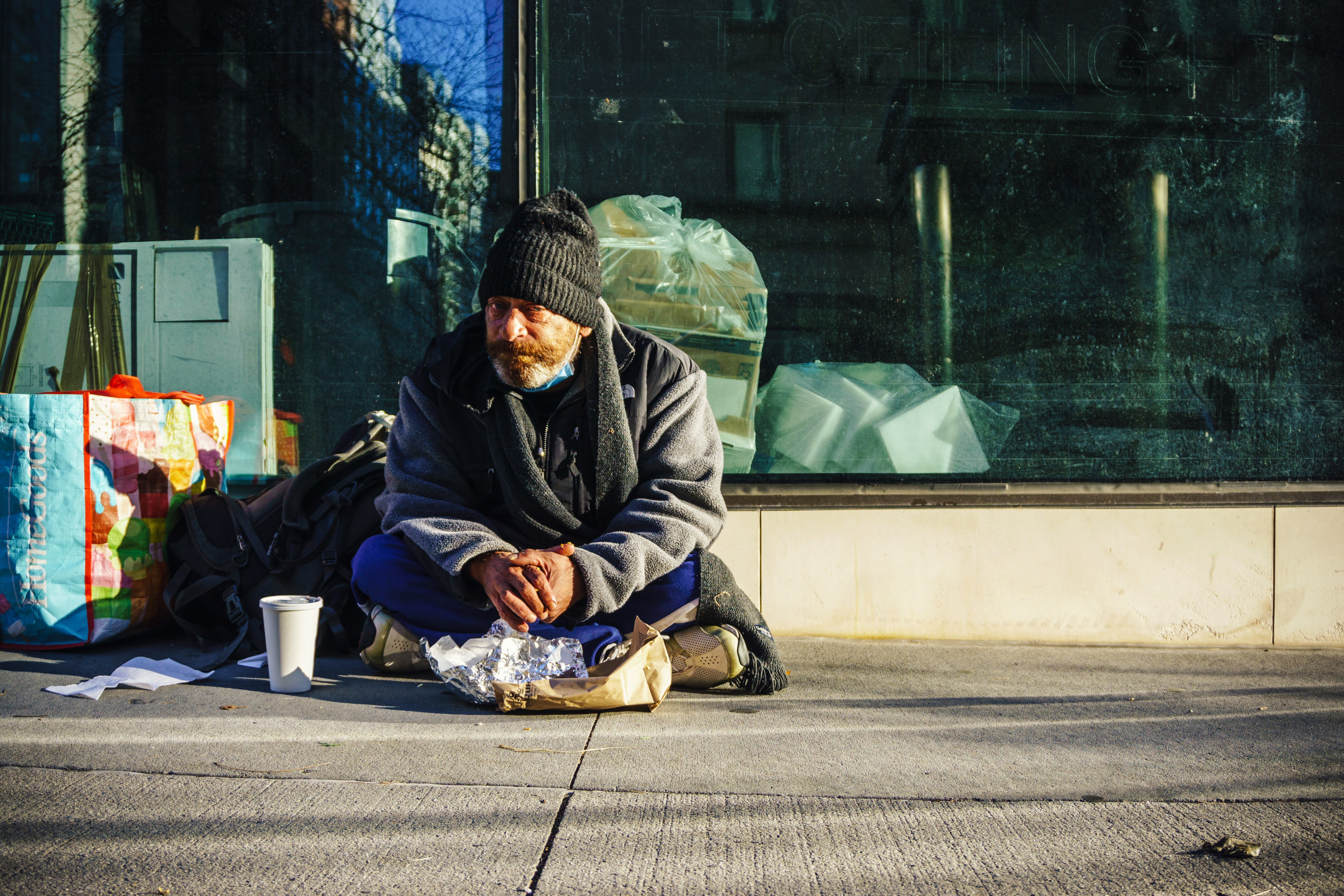 man in black and gray jacket sitting on sidewalk during daytime